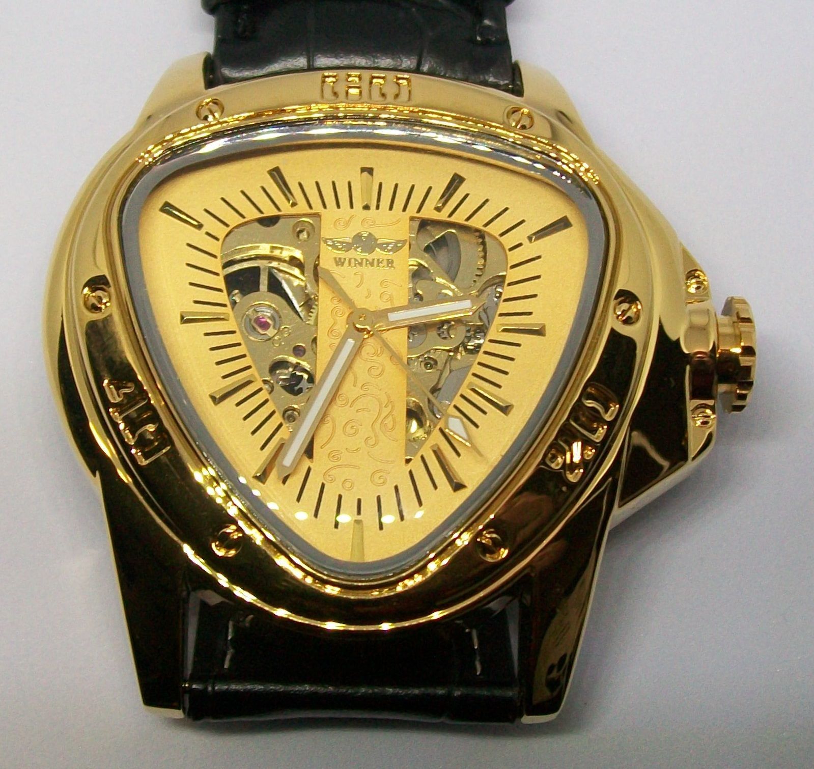 Gouden, driehoekig horloge met skeletachtige wijzerplaat, zwarte leren band en gouden accenten.