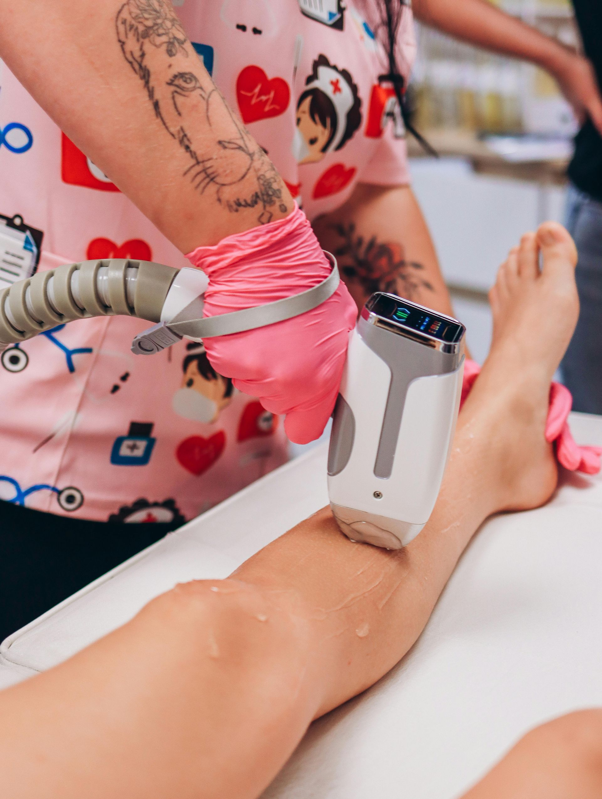 A professional uses a laser hair removal device on a person's lower leg in a clinic setting.
