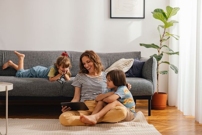 Woman with children reading a tablet on floor in living room.