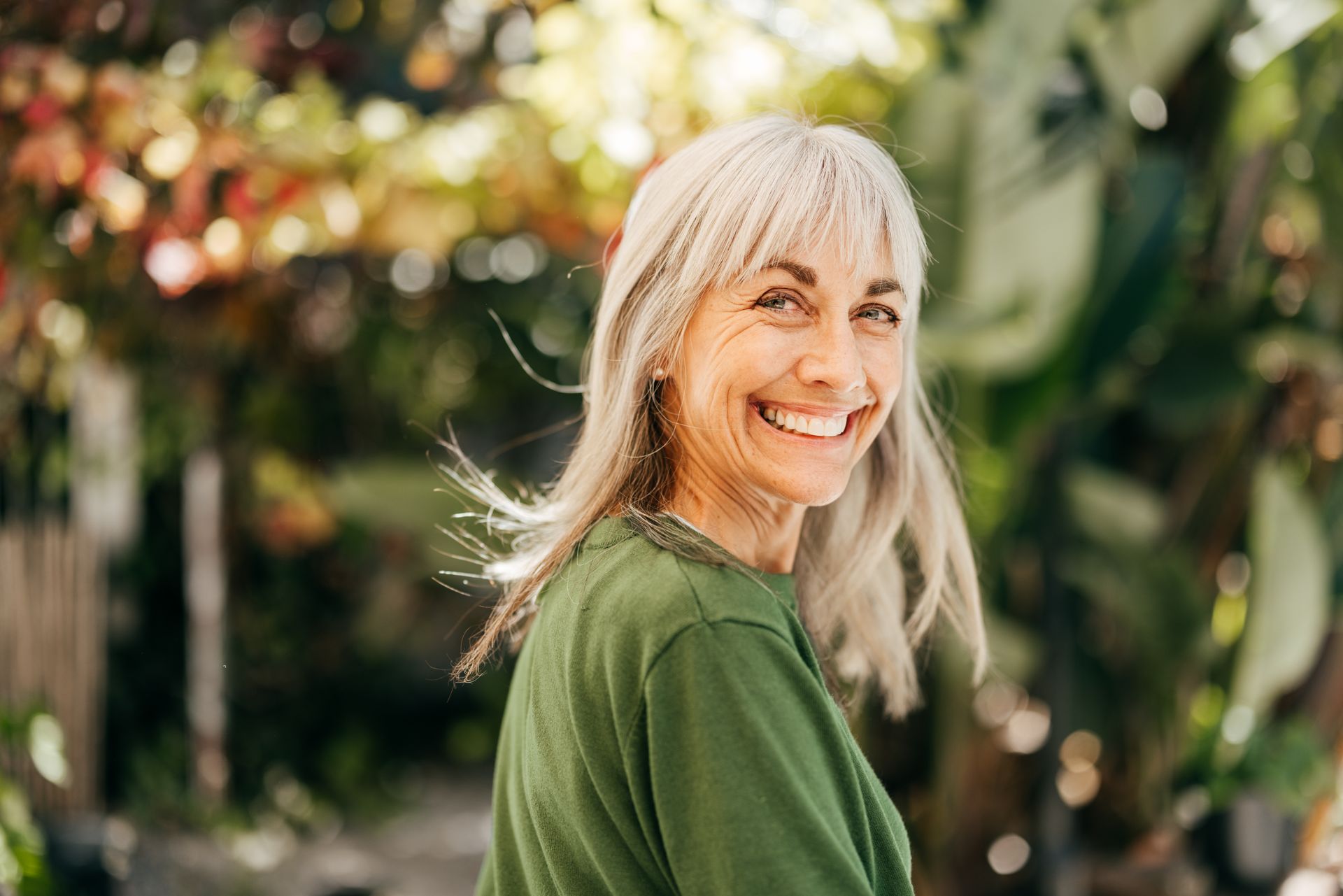Woman with long gray hair smiles outdoors in a green shirt.