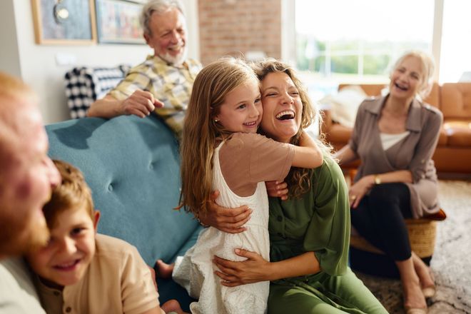 Family members laughing and hugging indoors on a couch.