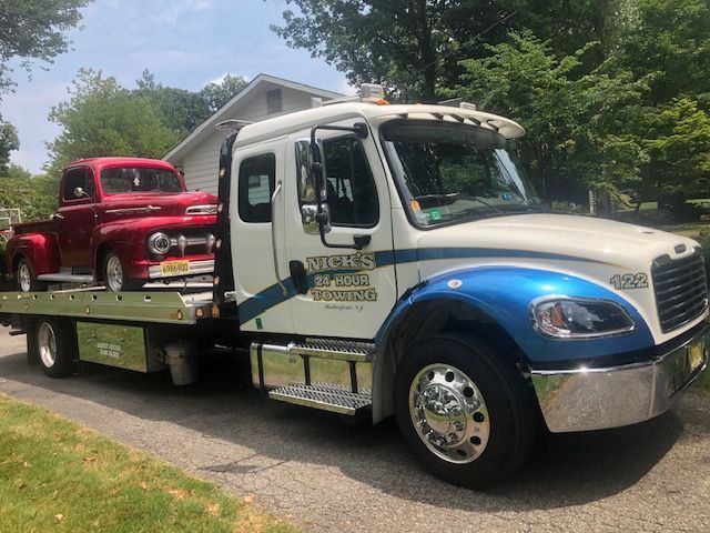 Nick’s Towing flatbed hauling vintage red pickup in Bergen County NJ neighborhood.