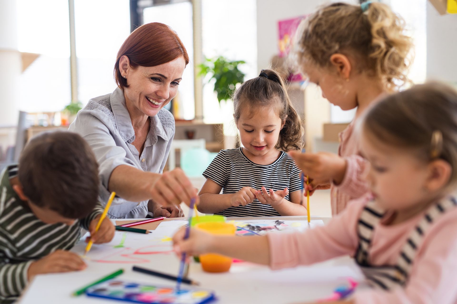 A group of children painting with a teacher indoors in a classroom. A group of children painting with a teacher indoors in a classroom.