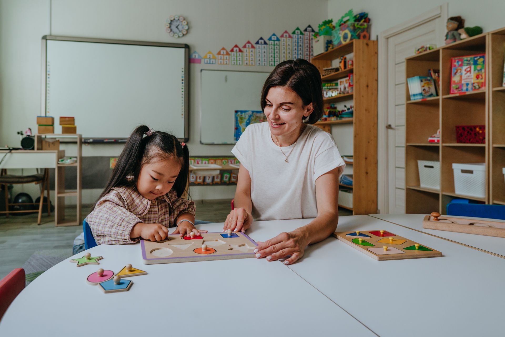 A woman and child playing with puzzles in a classroom, part of the toddler program activities.