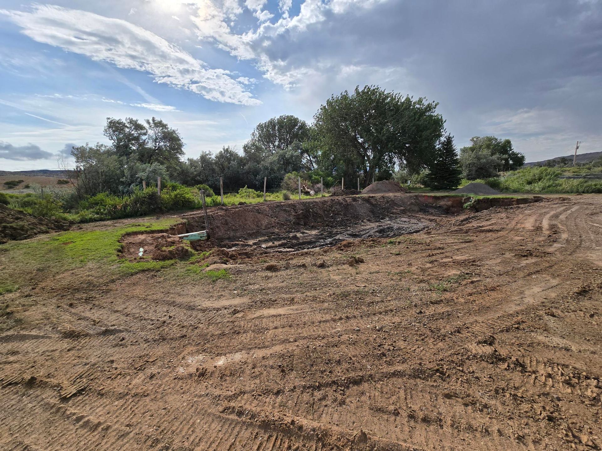 Earthworks and trees under a cloudy sky; construction site preparation.