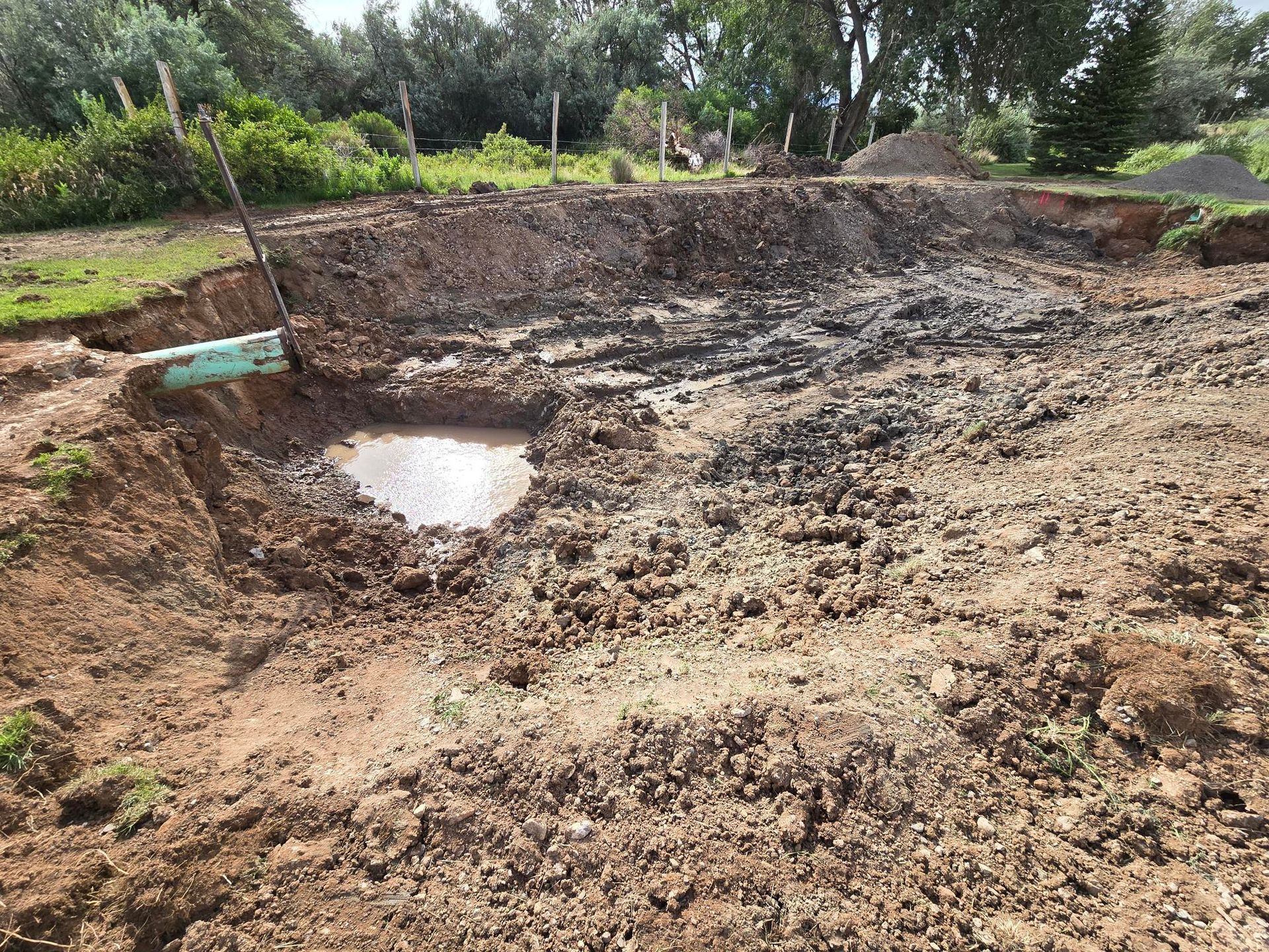 A muddy excavation site with a pipe and a puddle of water.