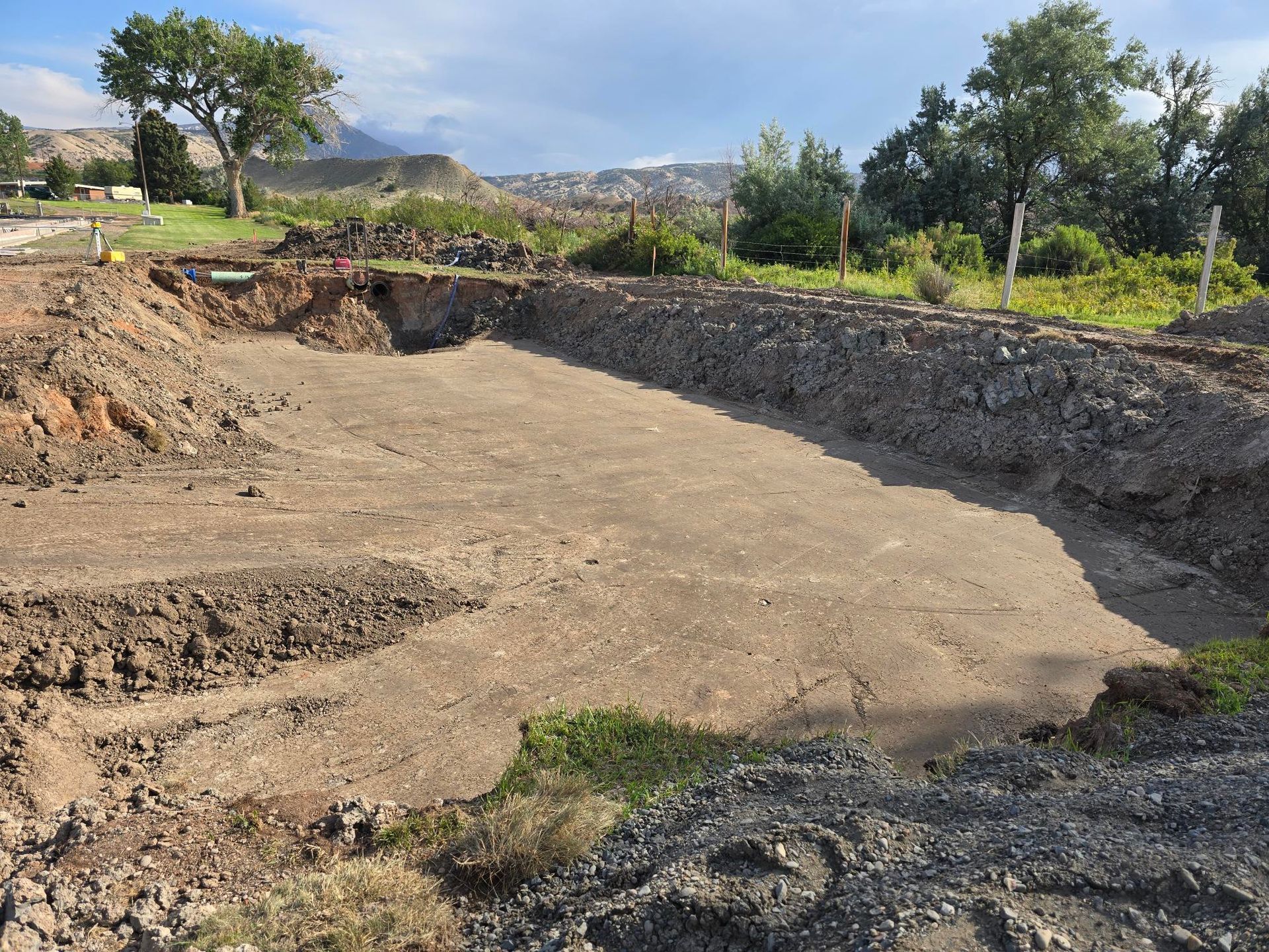 A large rectangular hole in the ground, ready for construction, with dirt piles around it.