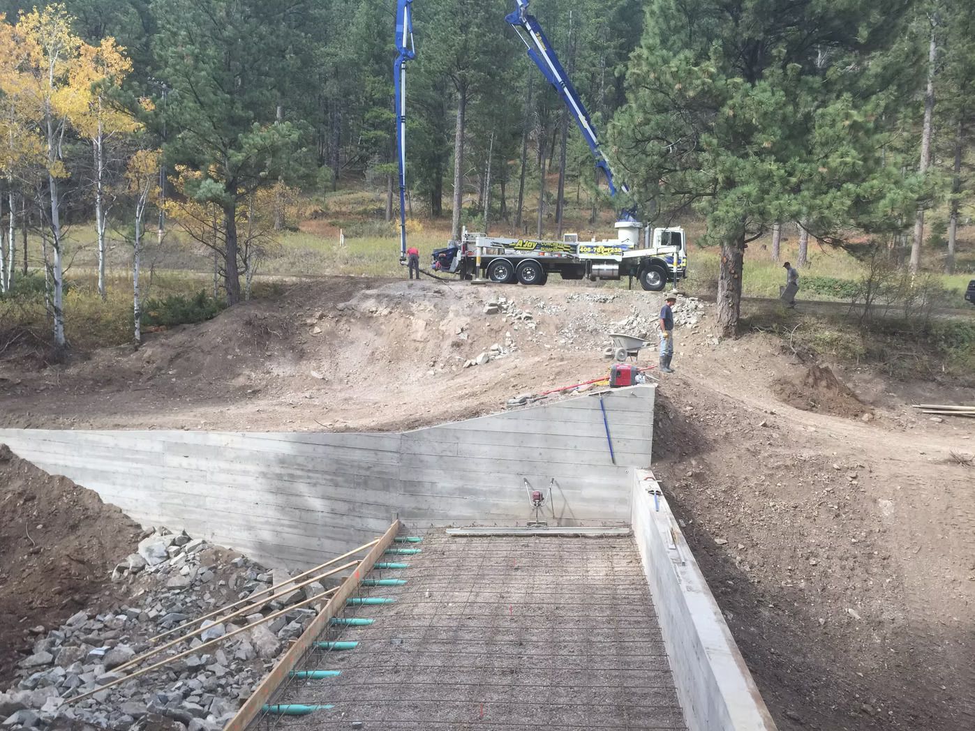 Concrete being poured for a bridge construction; truck with boom, workers, and natural setting.
