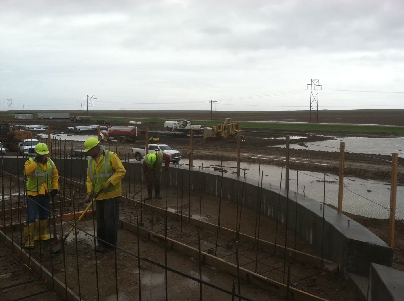 Construction workers building a curved concrete structure outdoors on an overcast day.