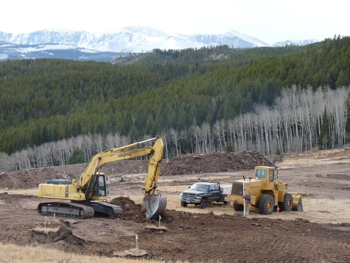 Excavator and loader on a construction site with a mountainous backdrop.