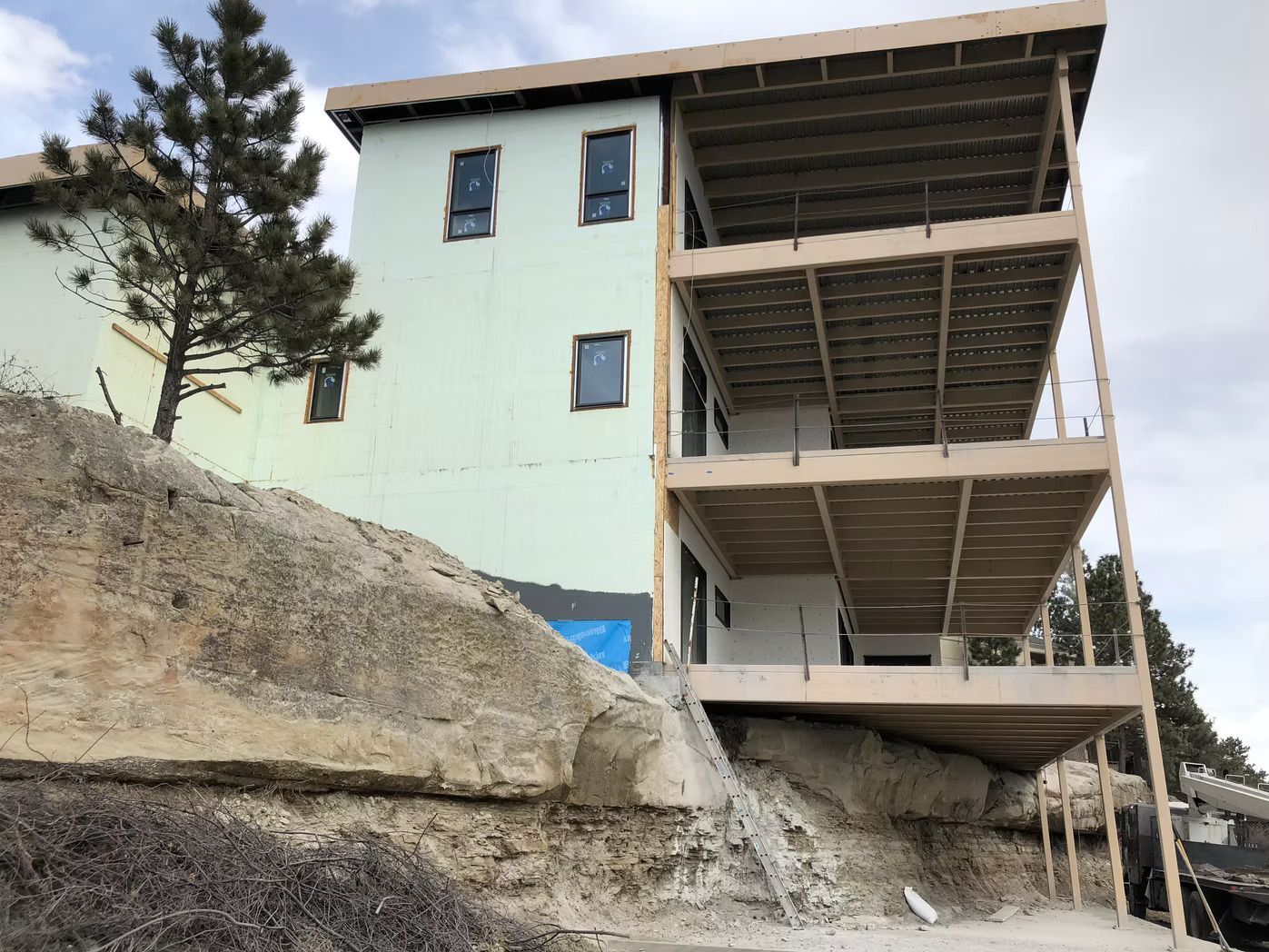 Multi-level building under construction on a rocky hillside. Light green exterior, wood framing.
