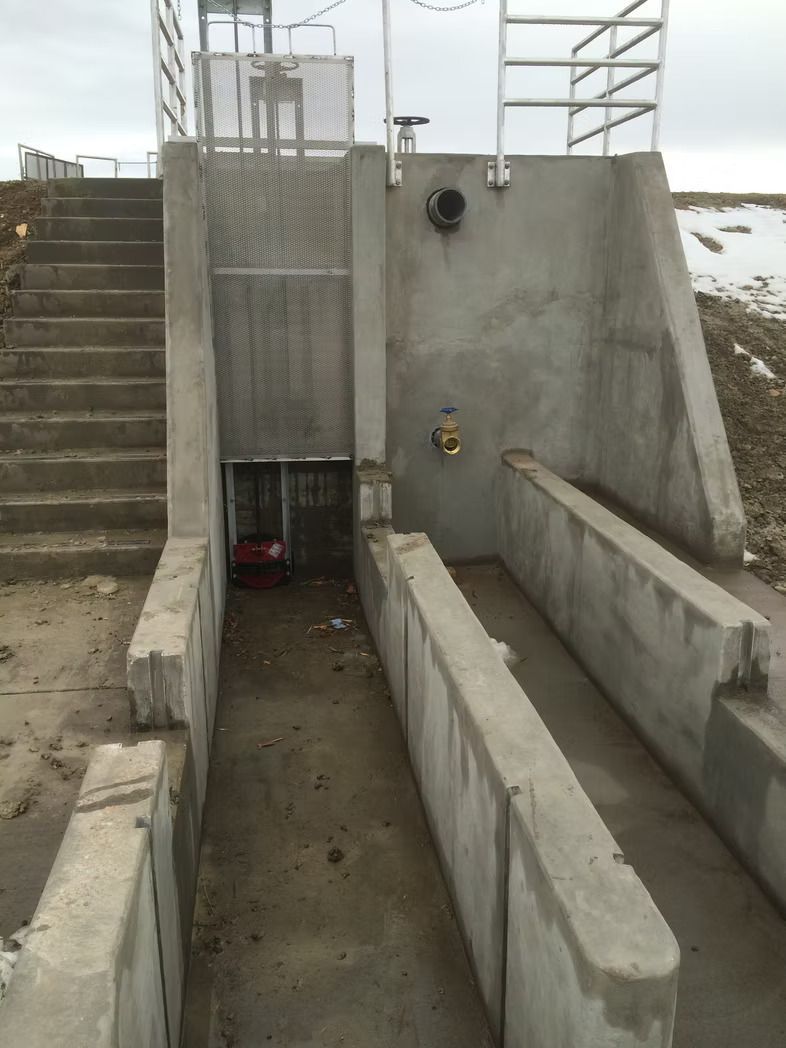 Concrete structure with steps, metal grate, and ramp-like channels; possible water control system.