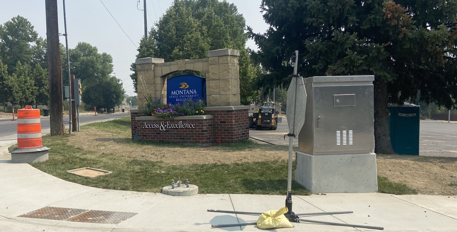Entrance sign to a city with a brick base, a blue crest, and utility boxes on the side of the road.