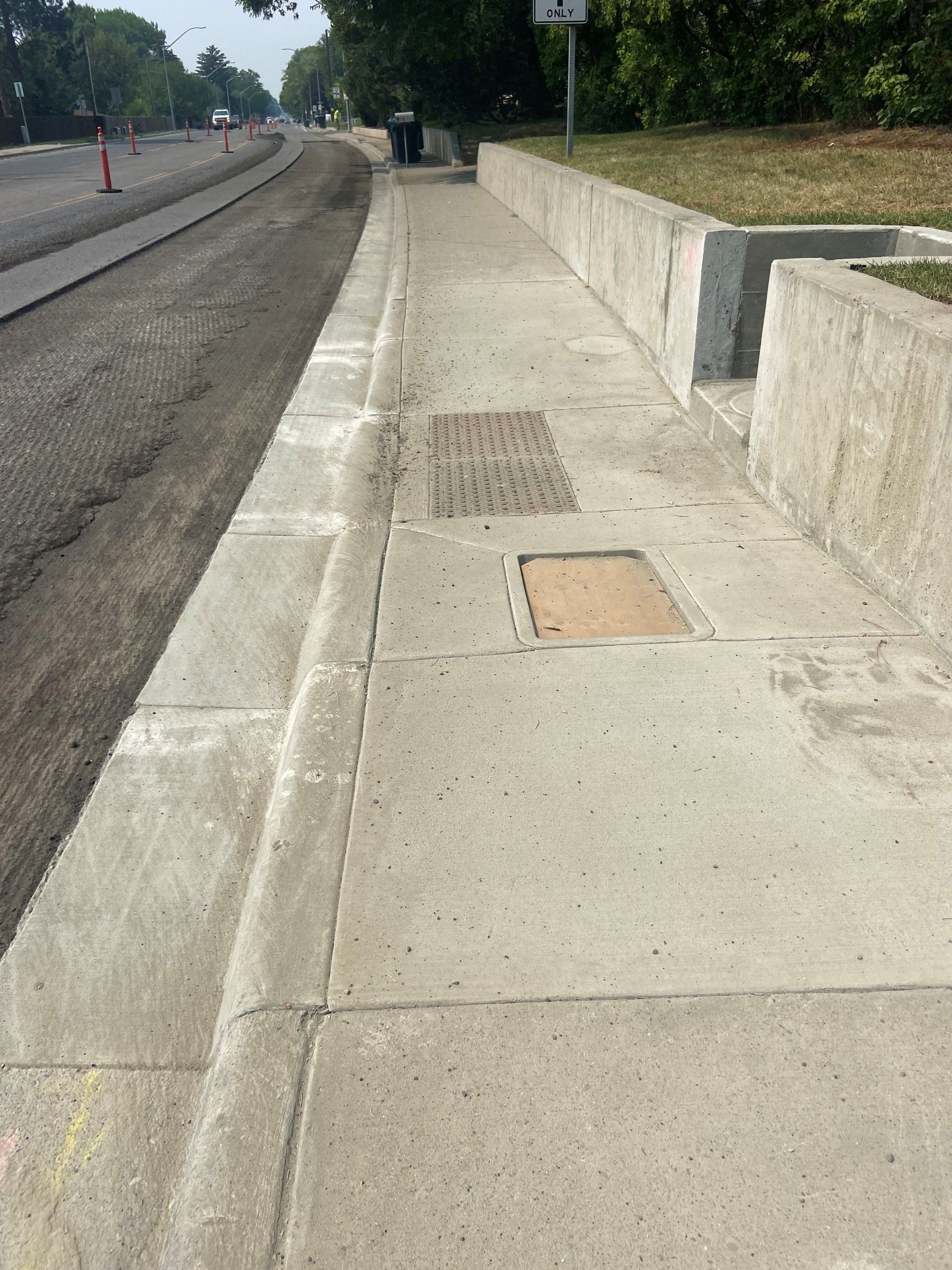 Concrete sidewalk next to a road under construction, with utility covers.