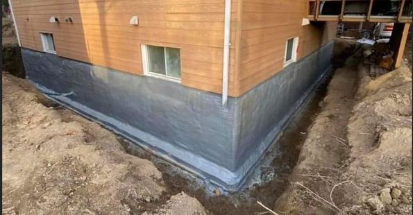 Les fondations d'une maison sont en train d'être imperméabilisées et peintes.