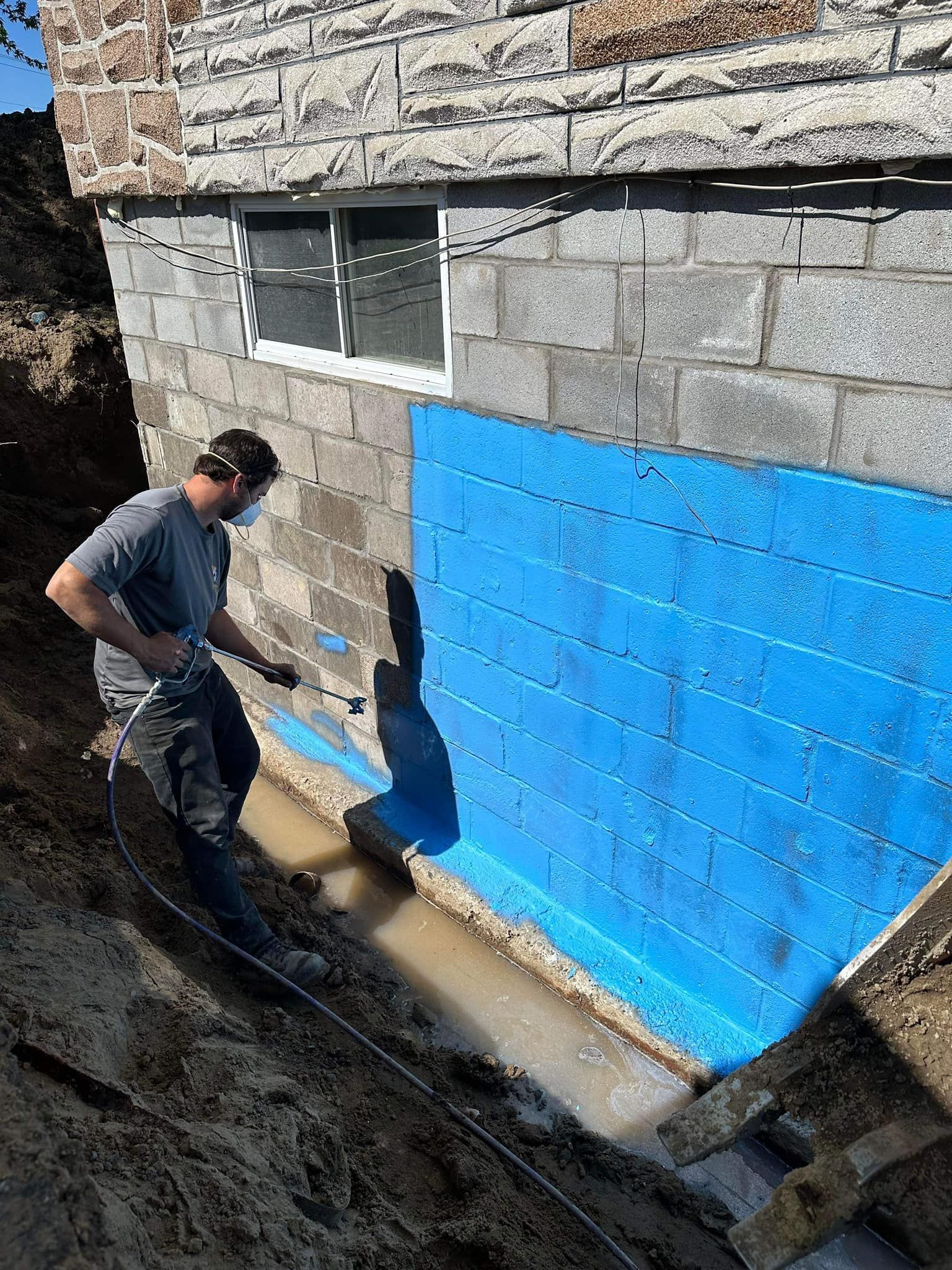 Un homme peint un mur de briques avec de la peinture bleue.
