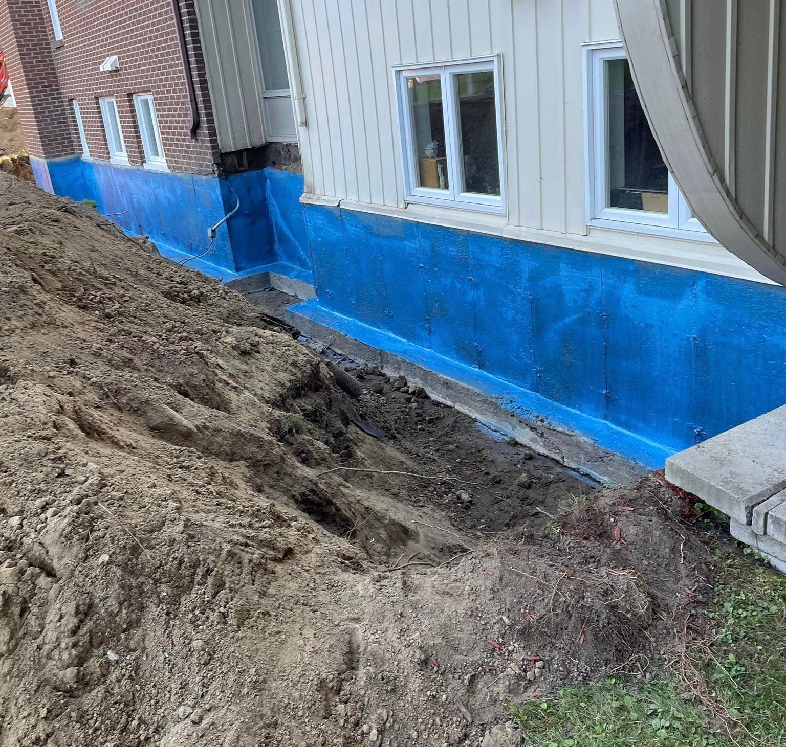 Membrane d'étanchéité bleue sur un mur de fondation d'une maison lors de travaux d'excavation.