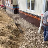 Un homme se tient à côté d'un tas de graviers devant une maison.