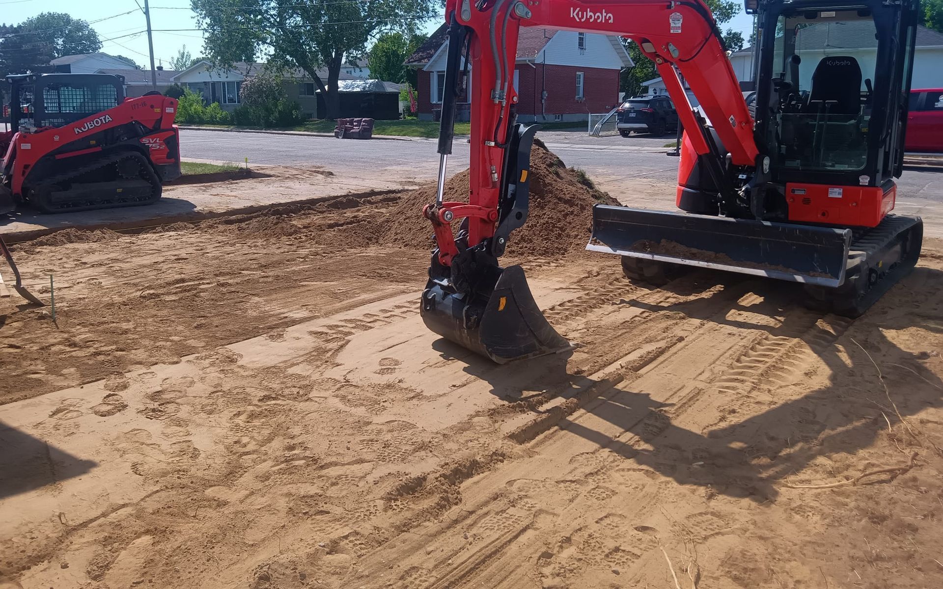 Excavatrice rouge creusant dans le sable avec une chargeuse compacte rouge en arrière-plan sur un chantier de construction.