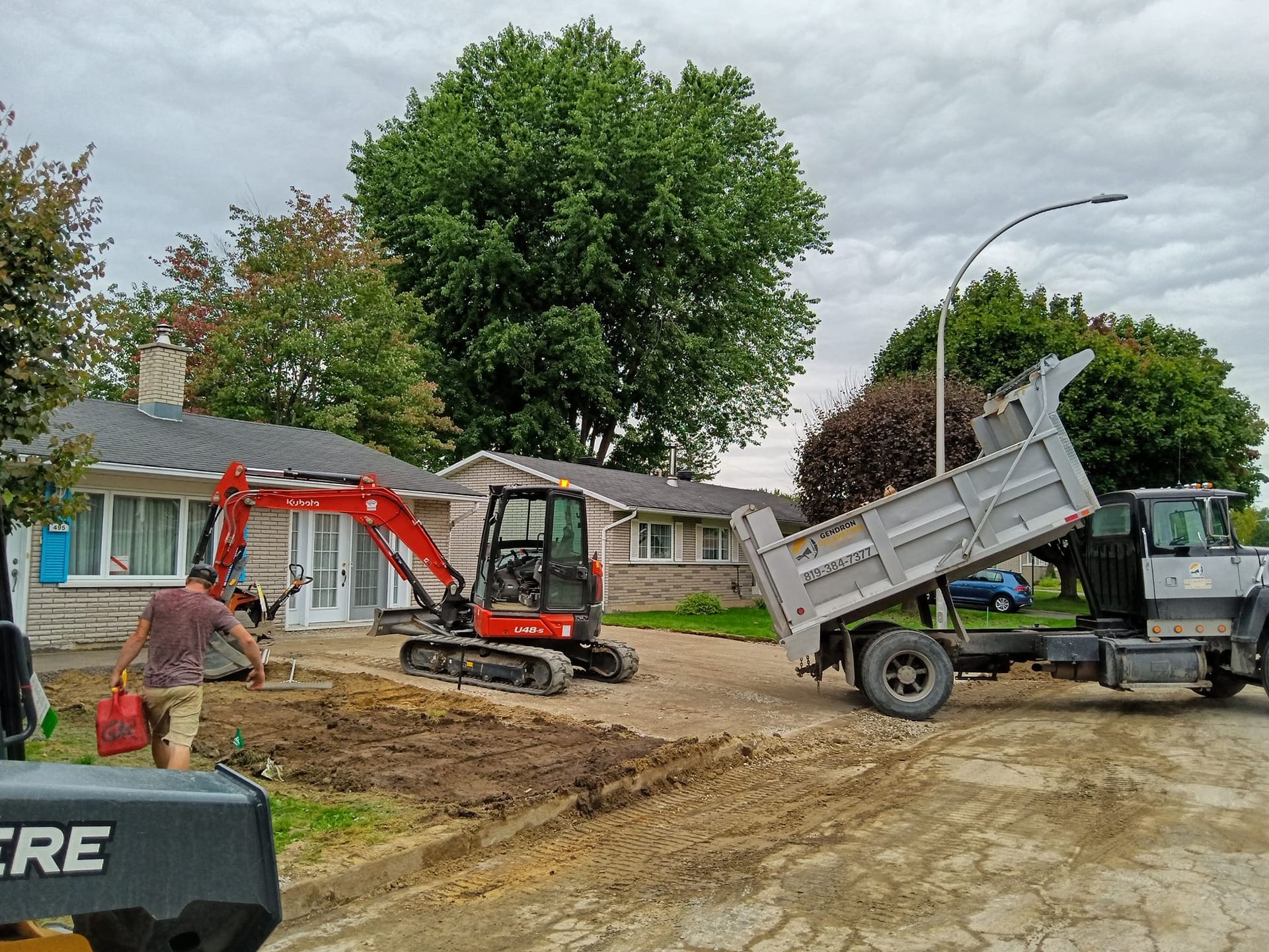Un camion-benne est chargé de terre devant une maison.