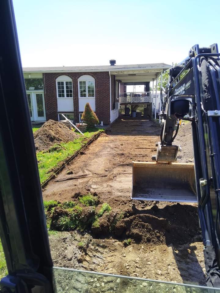 Une excavatrice déplace de la terre devant une maison en brique.