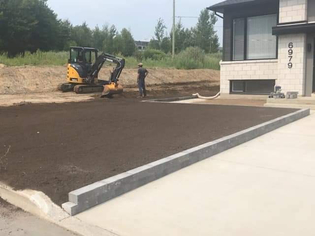 Un homme se tient à côté d'un bulldozer dans une allée devant une maison.