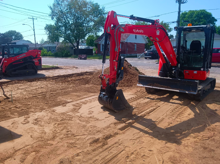 Une excavatrice rouge est assise au sommet d'un champ de terre.