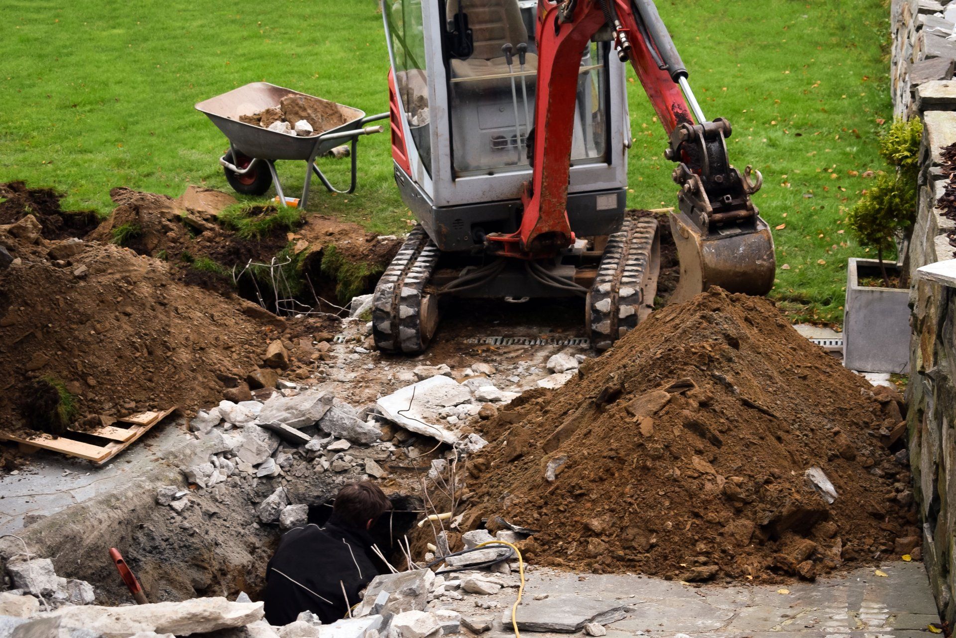 Une mini-pelle creuse dans une cour arrière ; des tas de terre et de débris entourent un trou.