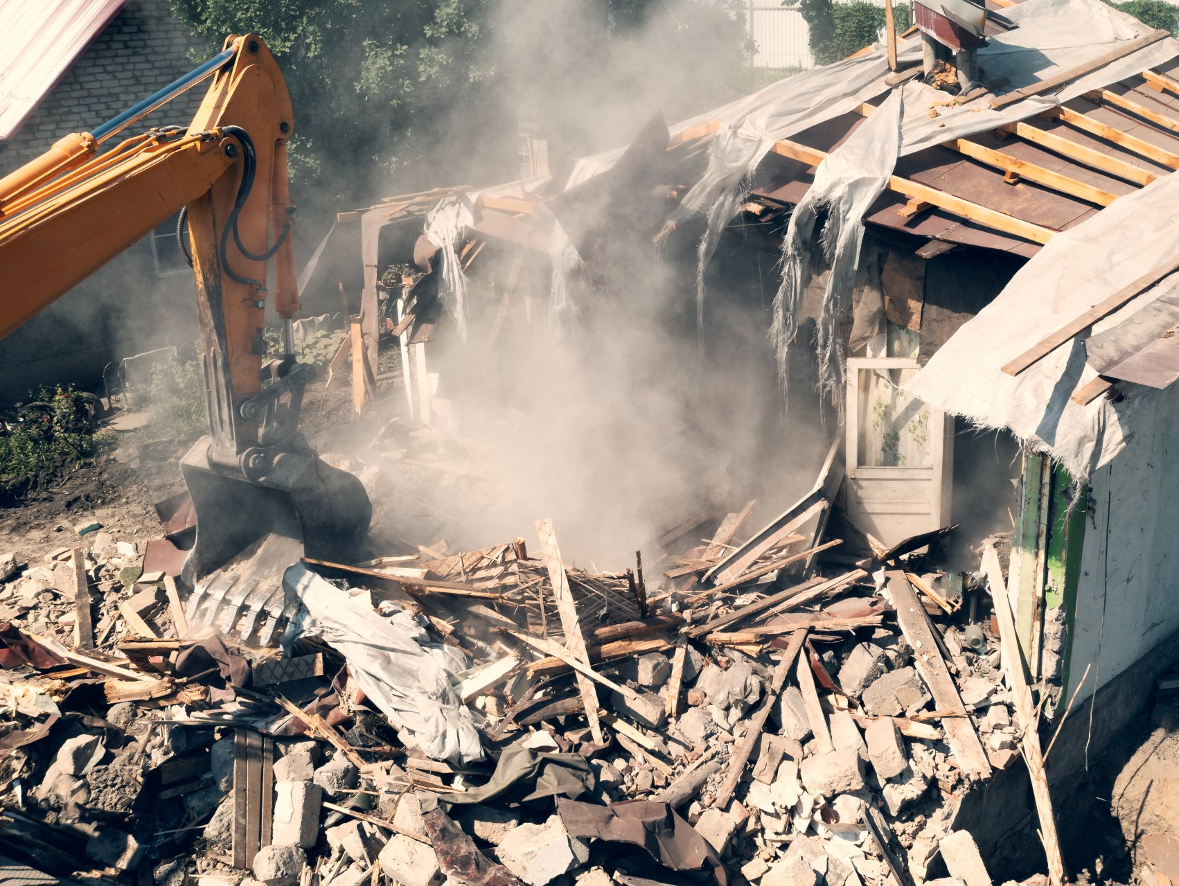 Une excavatrice jaune démolit une maison d'où sort de la fumée.