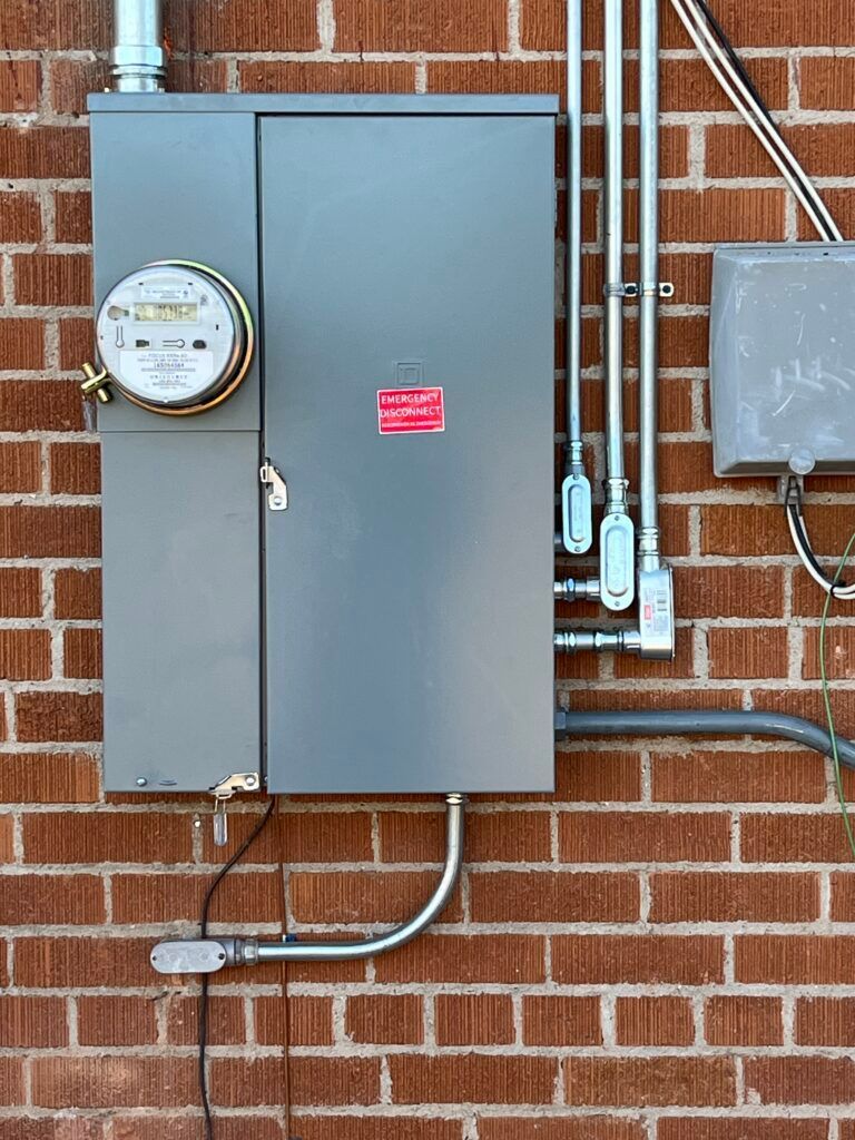 Electrical meter and panel on a red brick wall with conduit and wiring.