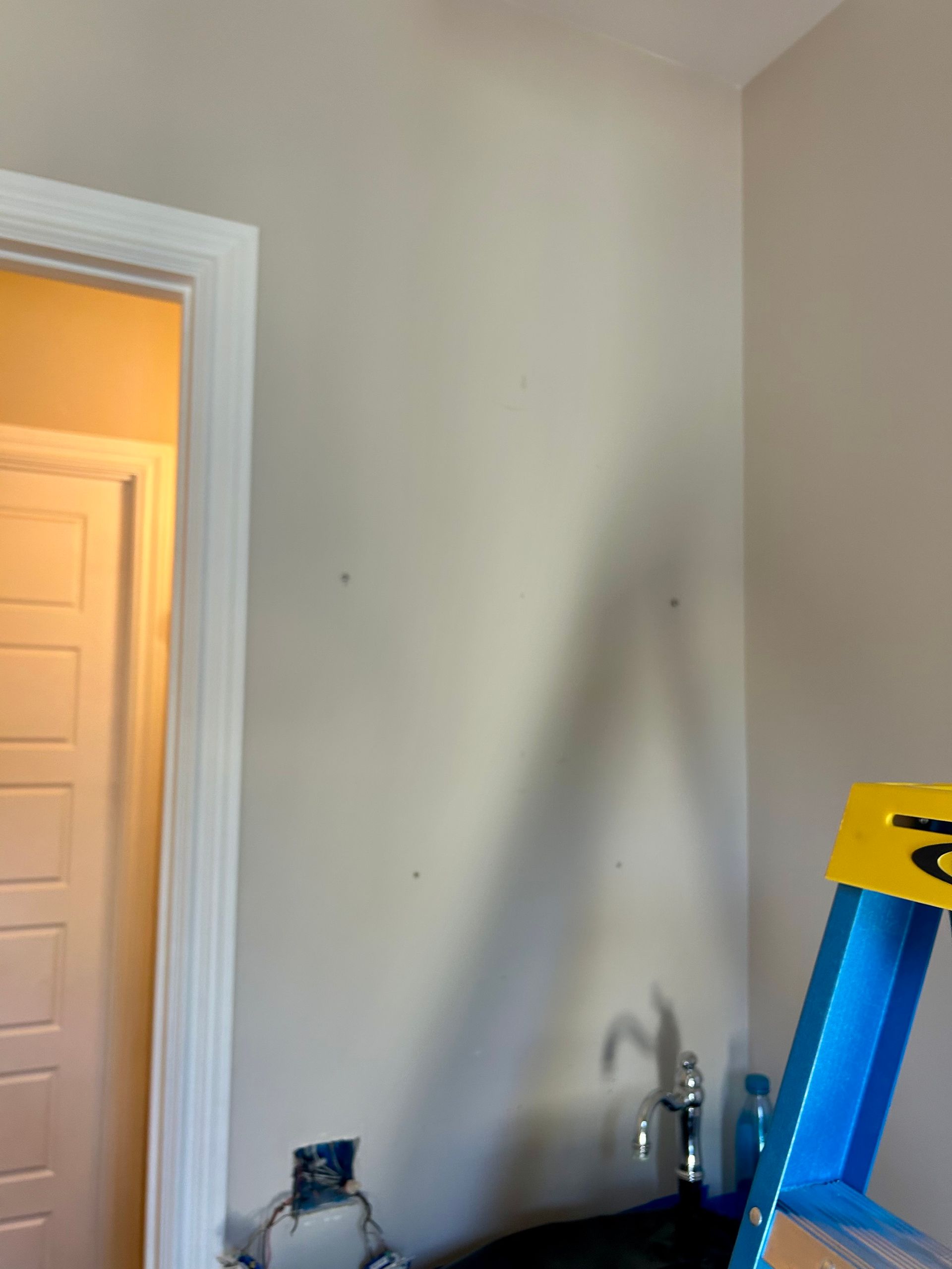 Interior wall with a doorway, dark sink, and blue ladder. Beige paint.