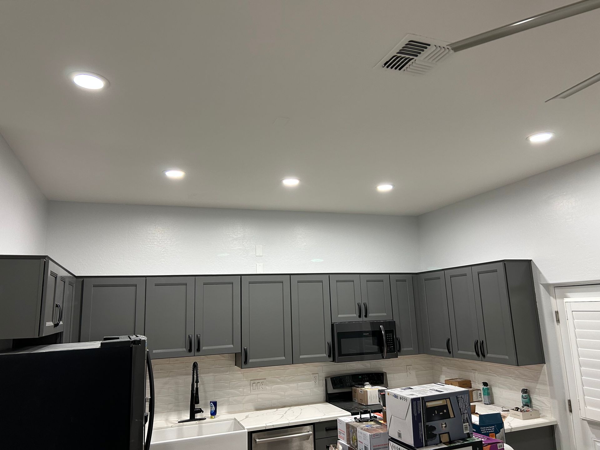 Gray kitchen cabinets with white countertop, underlit by recessed ceiling lights.