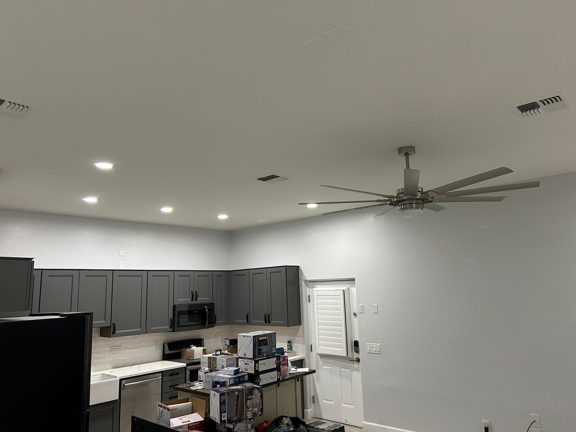 A kitchen with gray cabinets, a fan, and recessed lighting. Appliances and a door are visible.