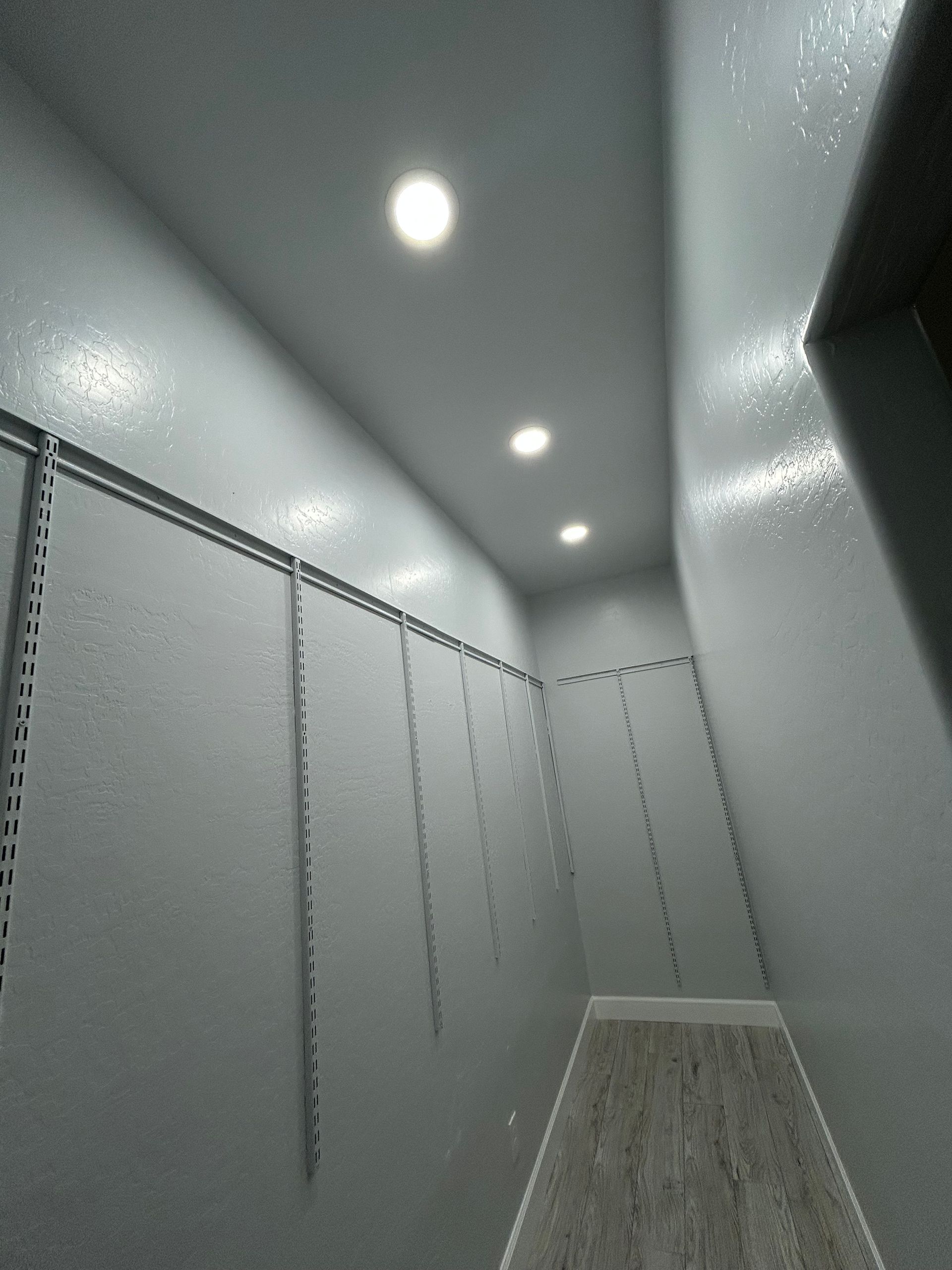 Narrow closet with gray walls, track shelving, and three recessed ceiling lights.