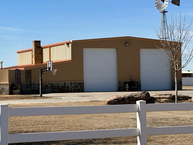A white fence surrounds a building with a windmill in the background