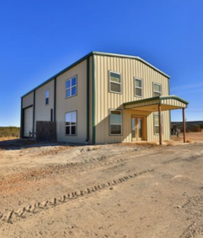 A large building with a green roof is sitting in the middle of a dirt field
