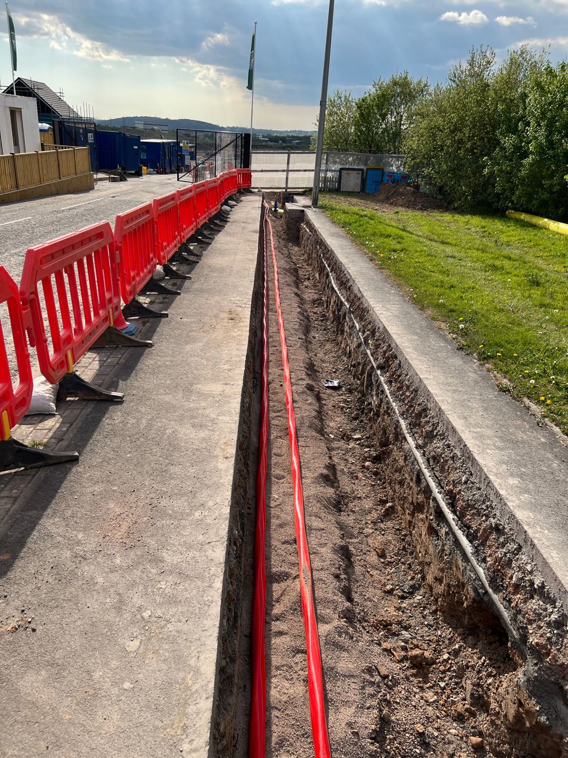 DP Cable Jointing | A row of red pipes are being installed in a trench next to a road.