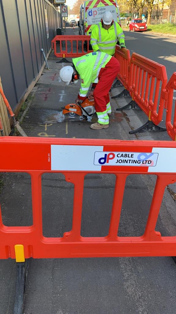 DP Cable Jointing | A man is cutting a hole in the ground behind an orange barrier.