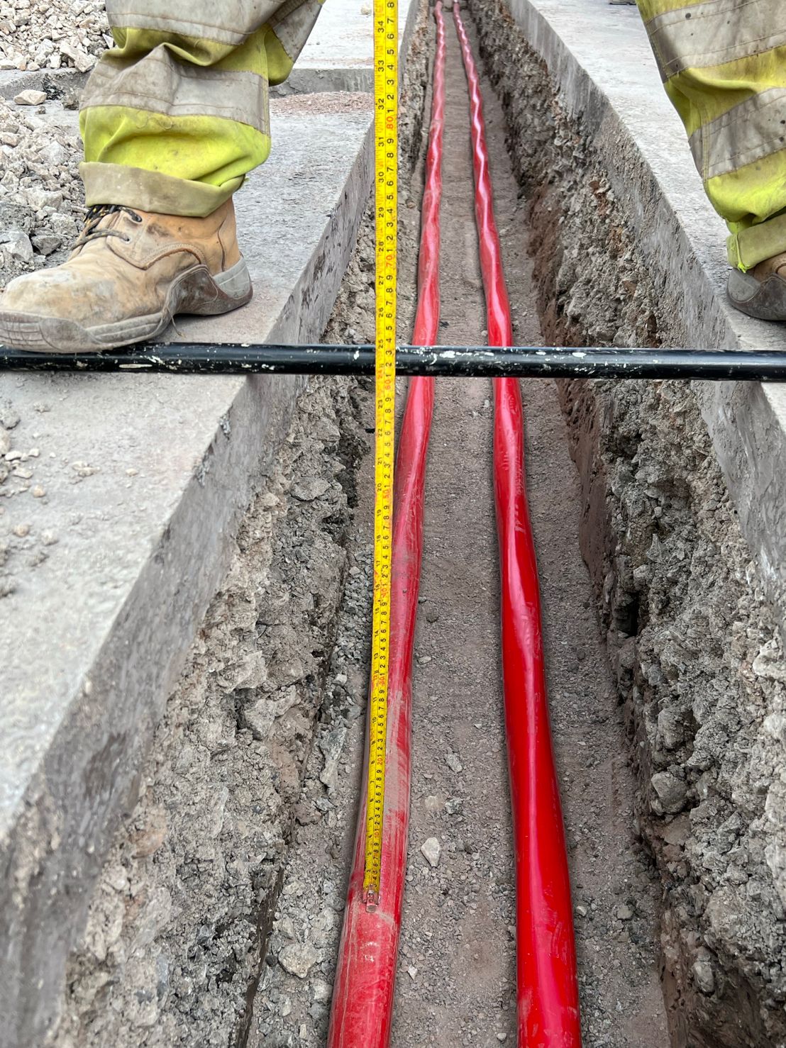 DP Cable Jointing | A person is measuring a red pipe in a trench with a tape measure.