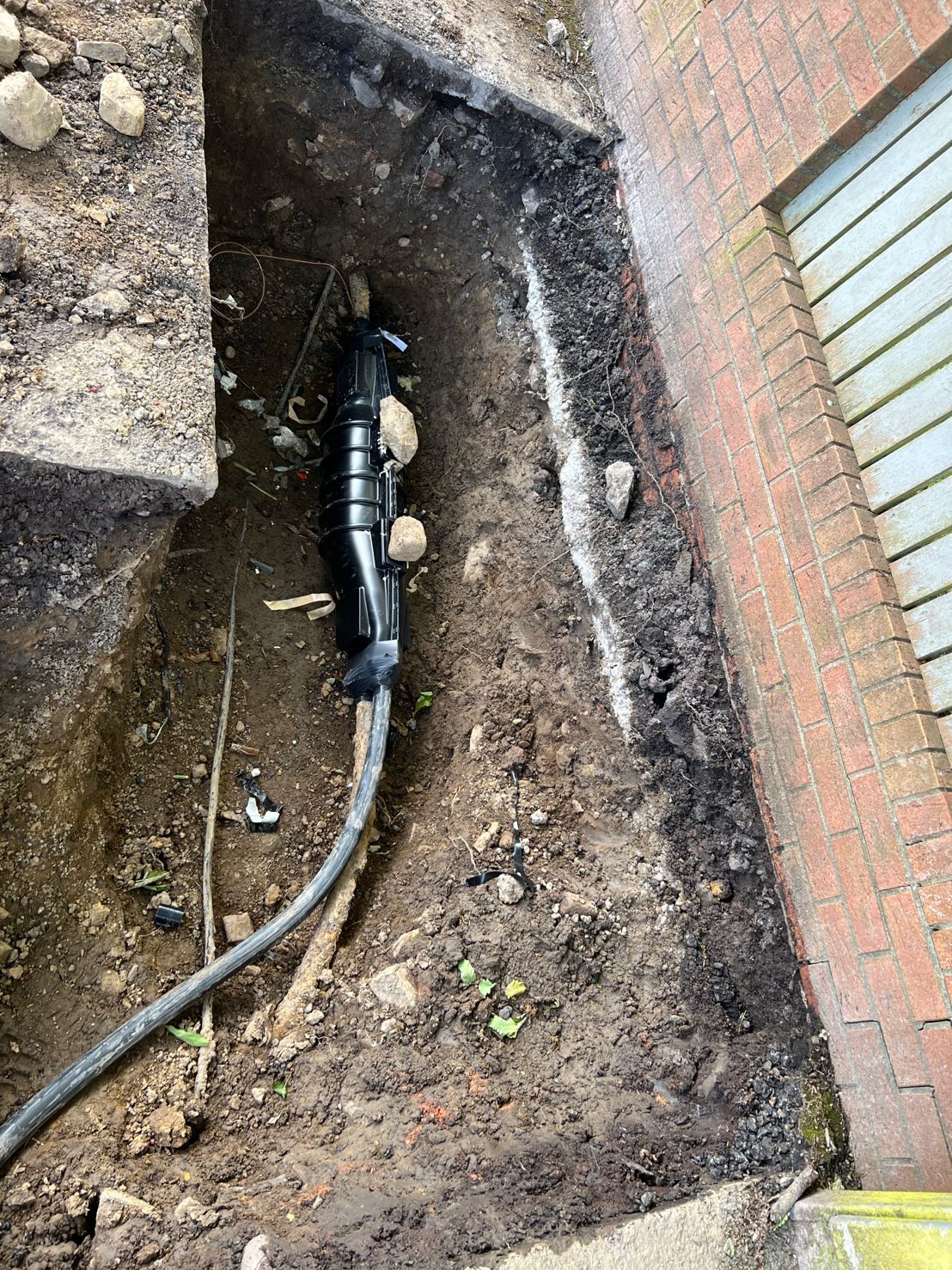 DP Cable Jointing | A hose is laying in the dirt next to a brick wall.