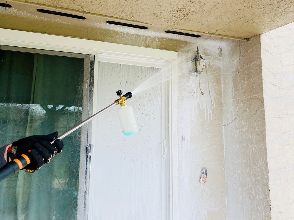 Person Wearing Gloves Sprays Foam on a White Door and Wall With a Pressure Washer — Ericson Constructions in Mareeba, QLD