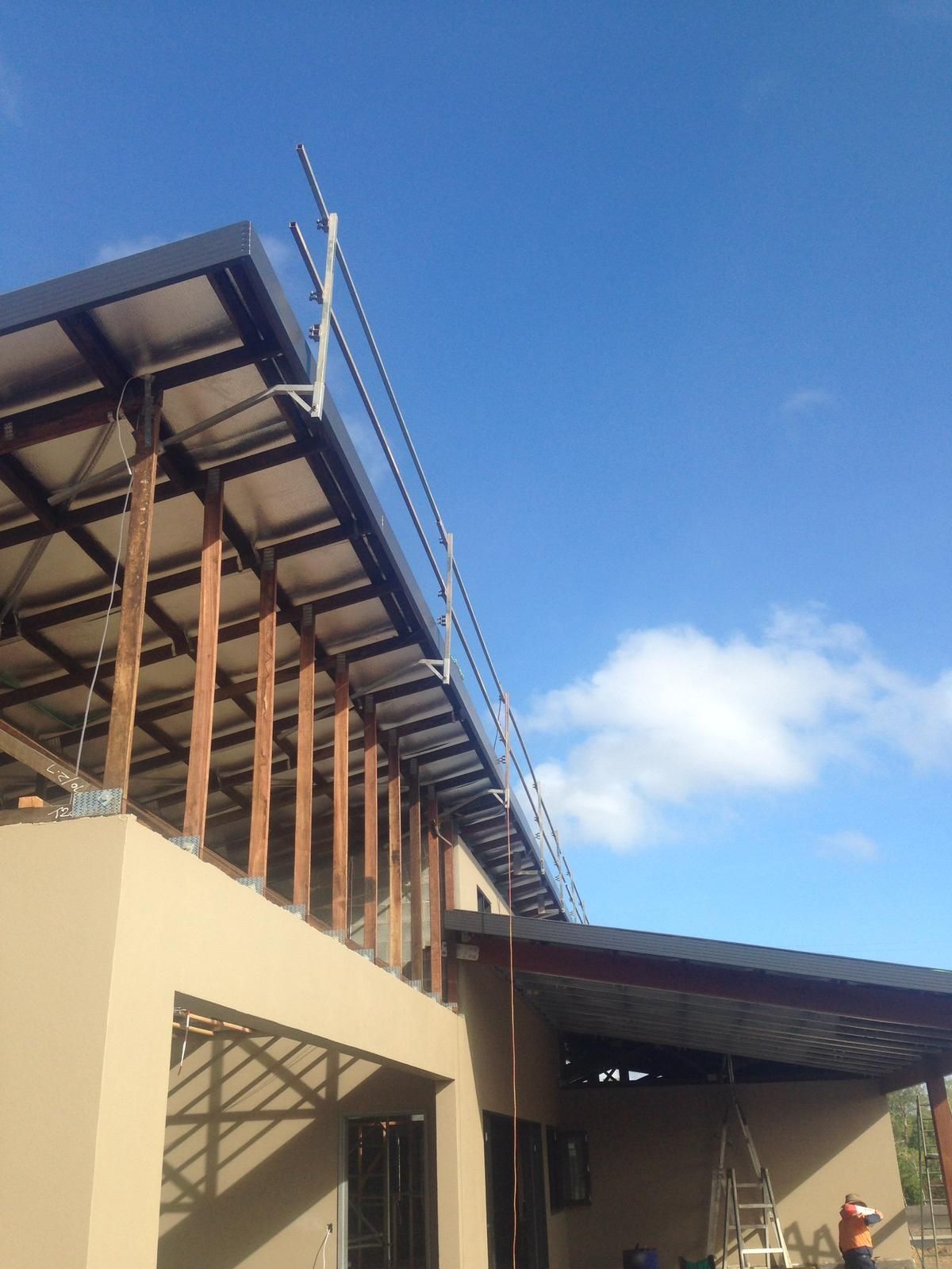 Beige and brown building under a blue sky, with a roof under construction and safety cables installed.