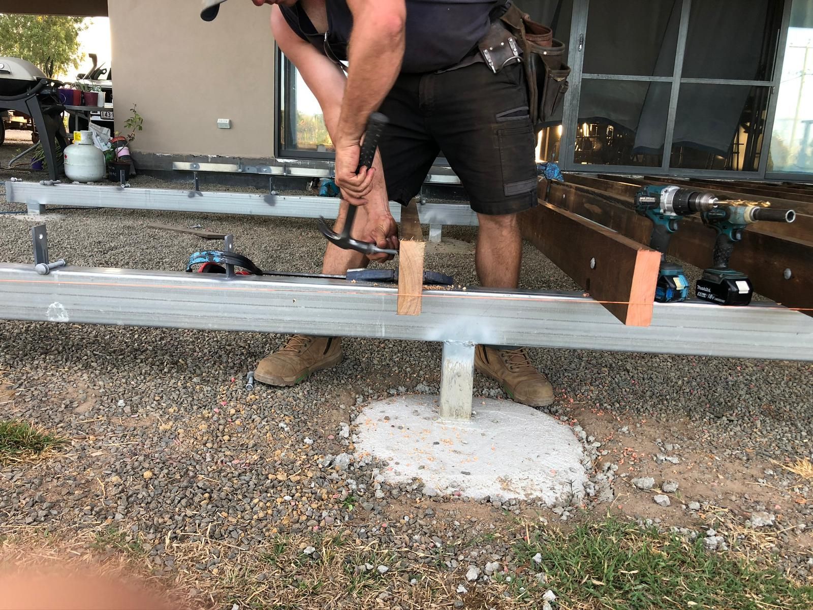 Person hammering wood on a metal frame, outdoor setting with a concrete base.