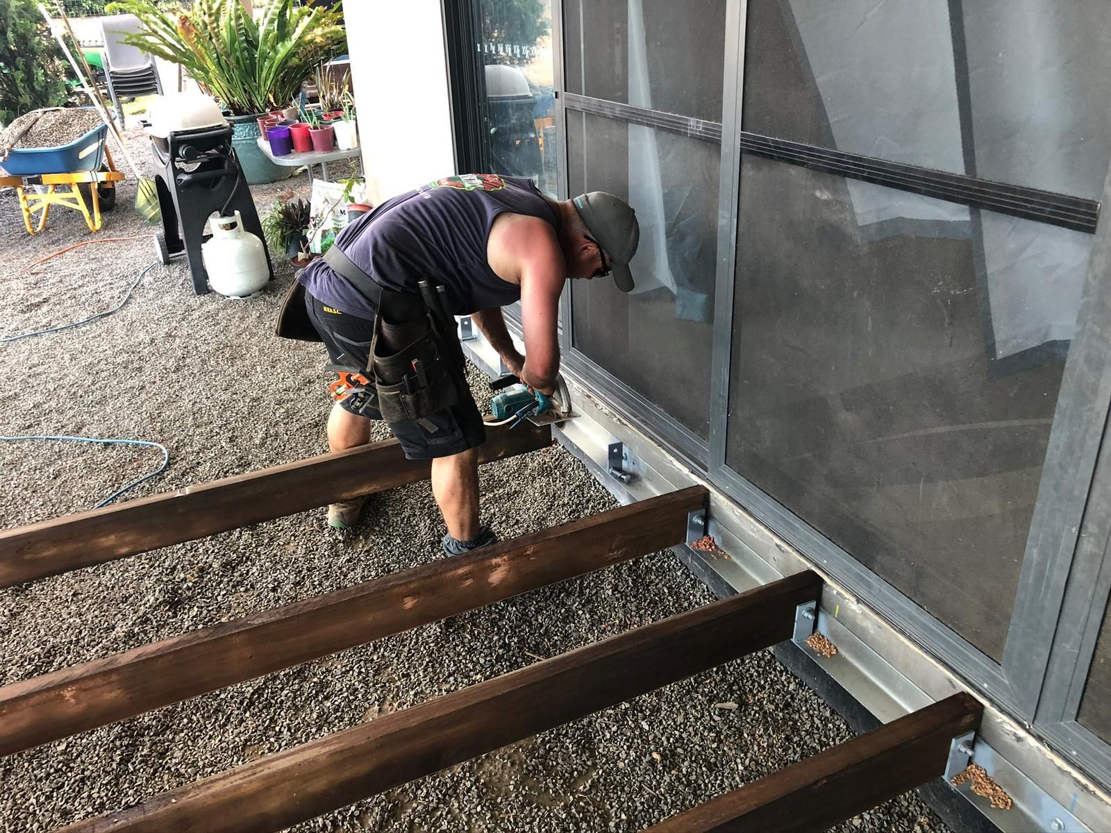 A person working on wooden deck boards, using a power tool outdoors.
