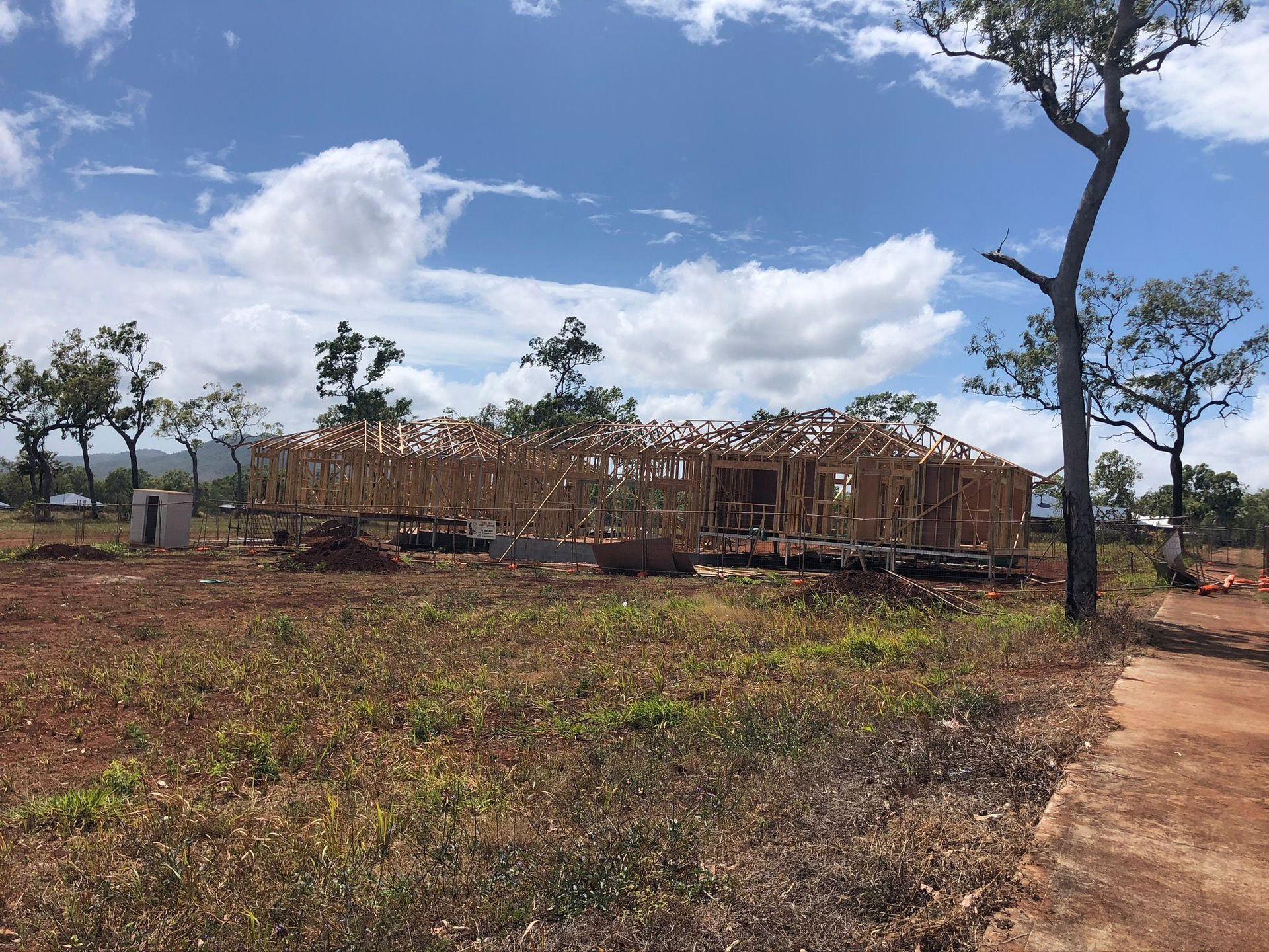 Building under construction, wooden frame visible, on a grassy field under a blue sky.