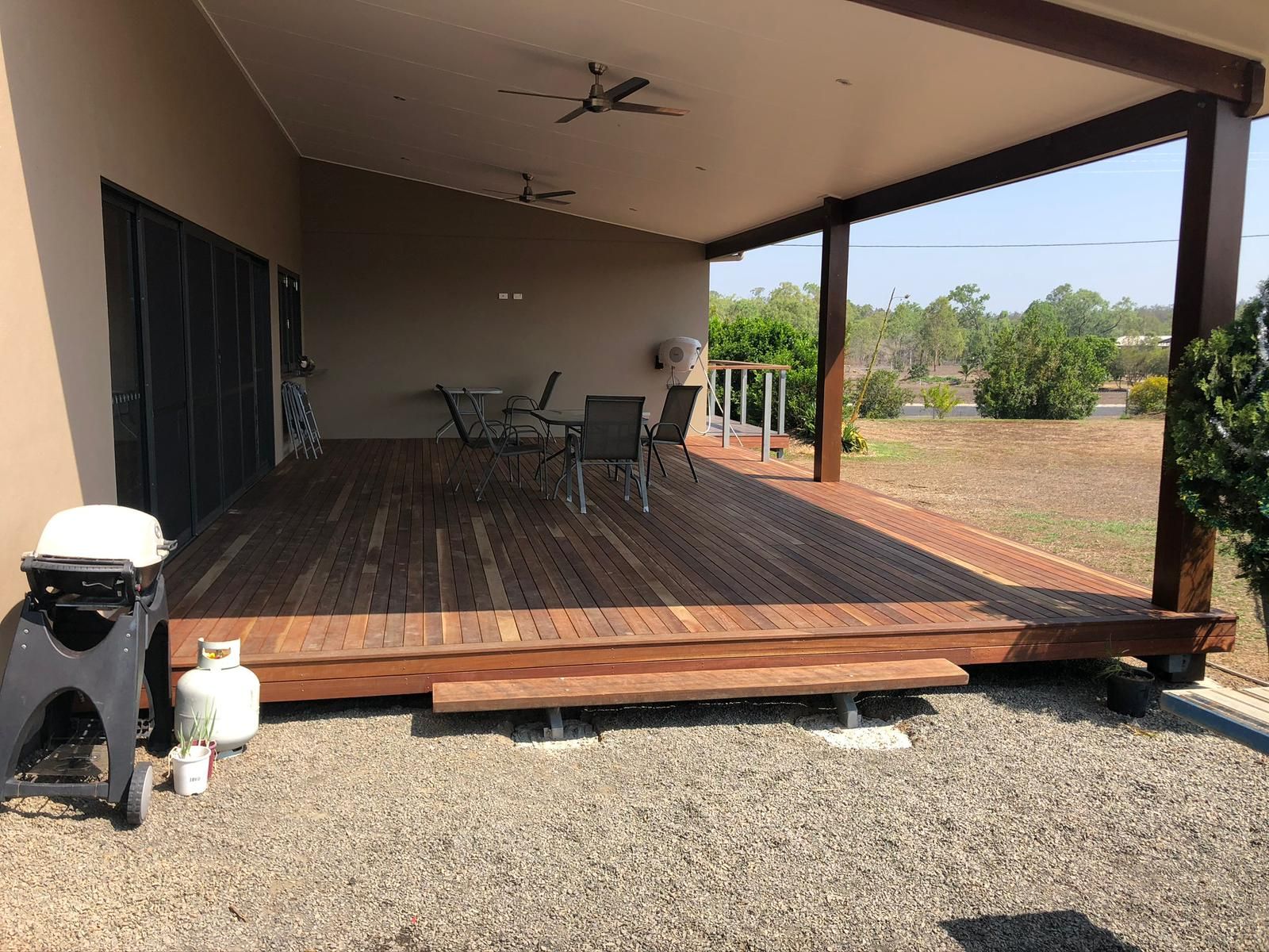 Covered wooden deck with outdoor furniture, grill, and gravel ground.