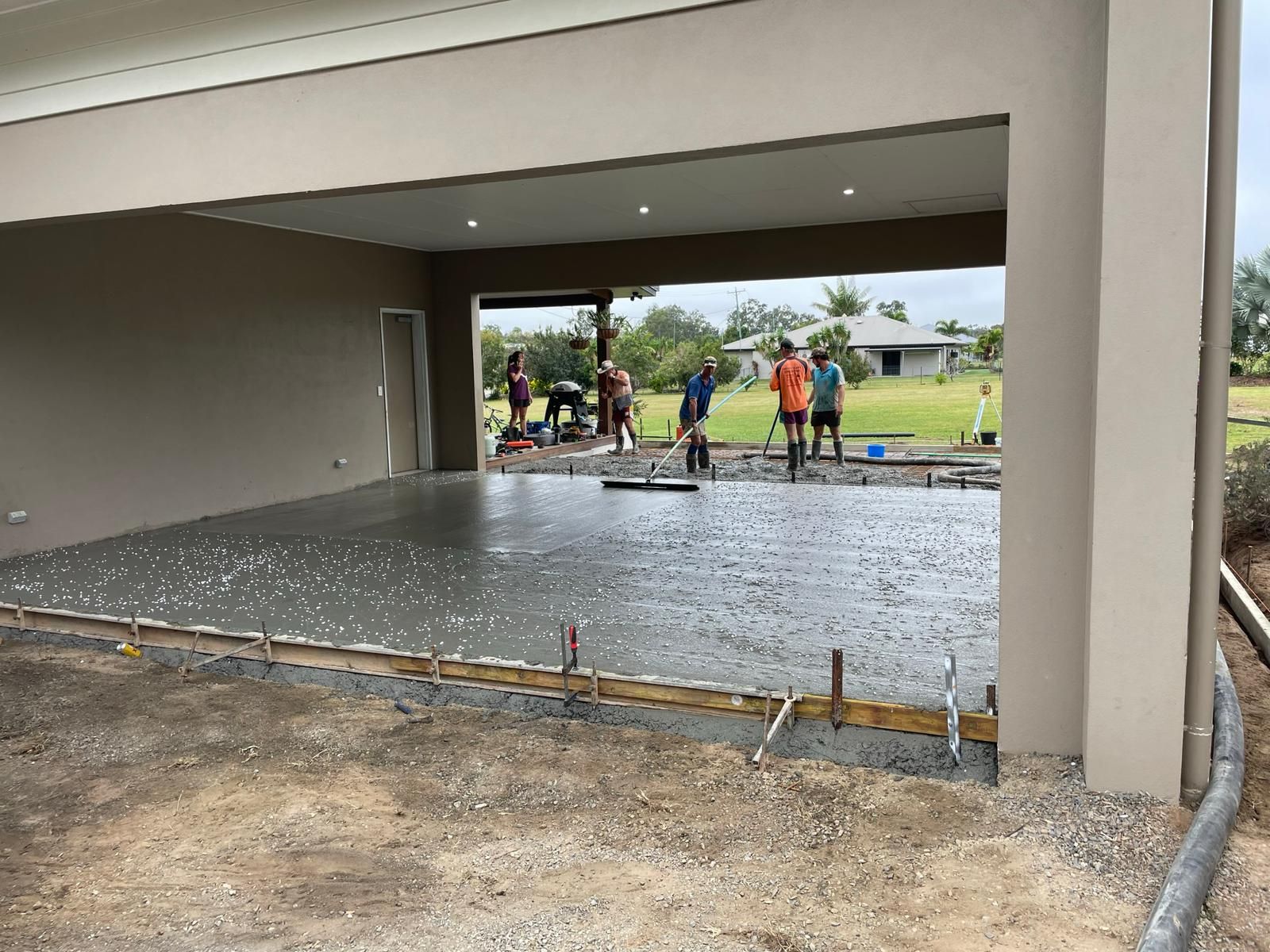 Construction workers pouring concrete slab under a roofed structure with outdoor view.