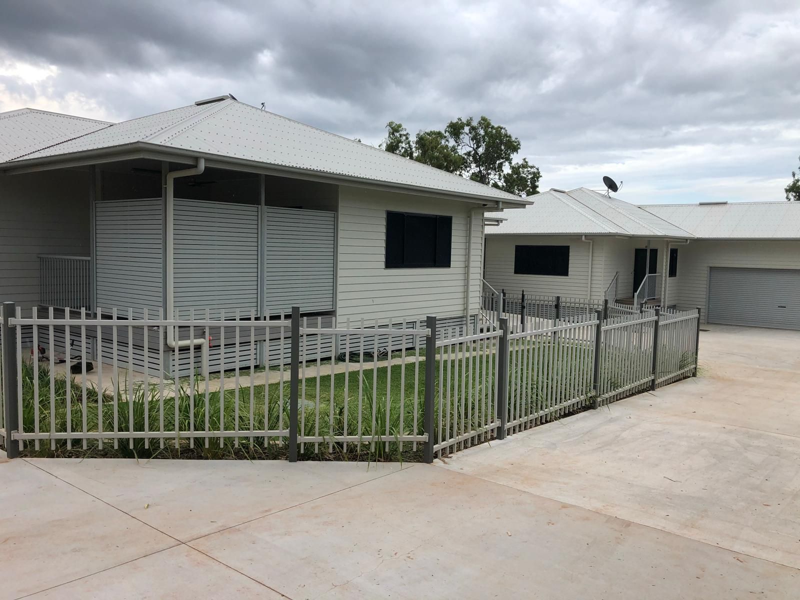 White buildings with metal roofs and a gray fence, under a cloudy sky.