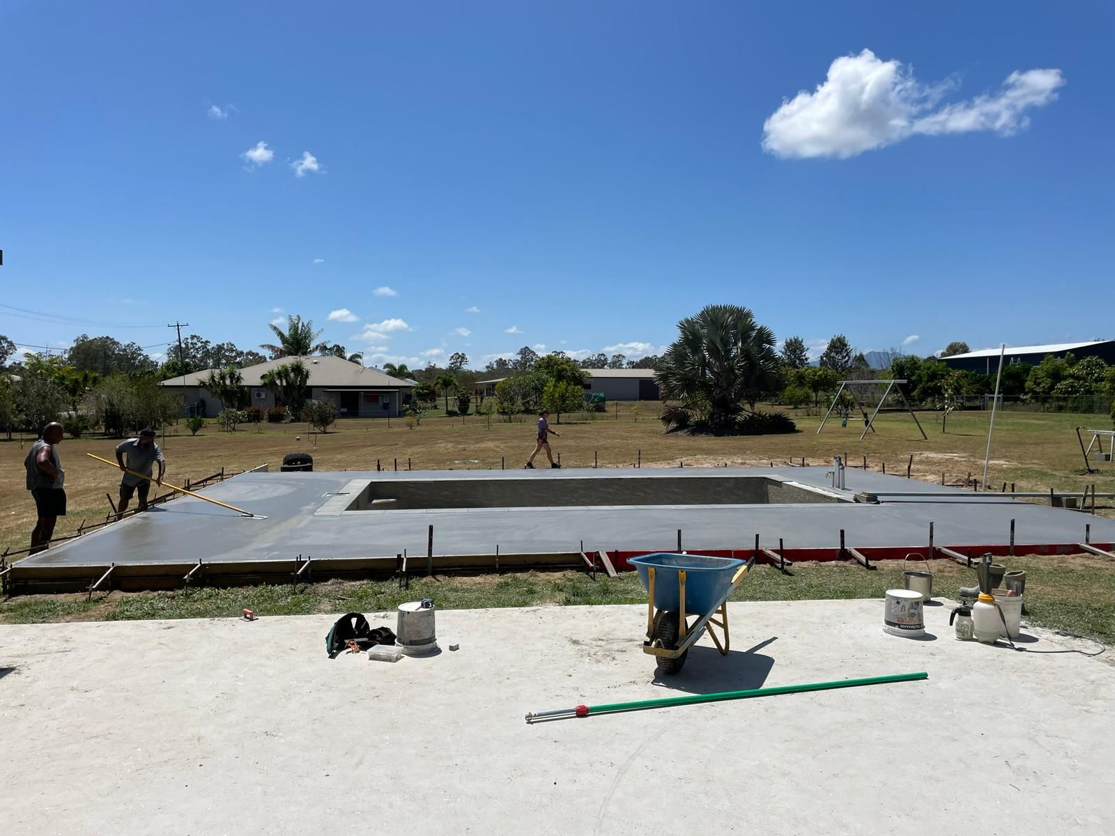 Pool construction in progress: concrete form, workers, tools, and a sunny, outdoor setting.
