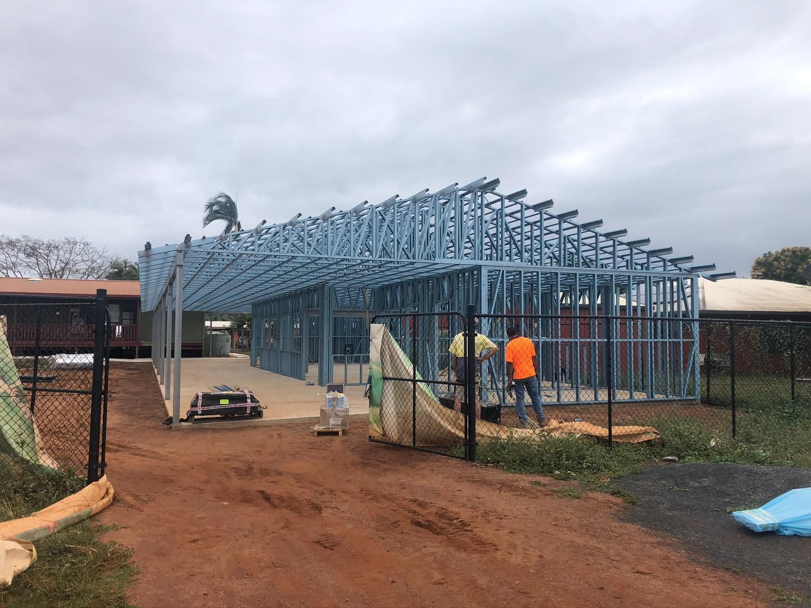 Construction site with a metal frame building in progress, two workers.